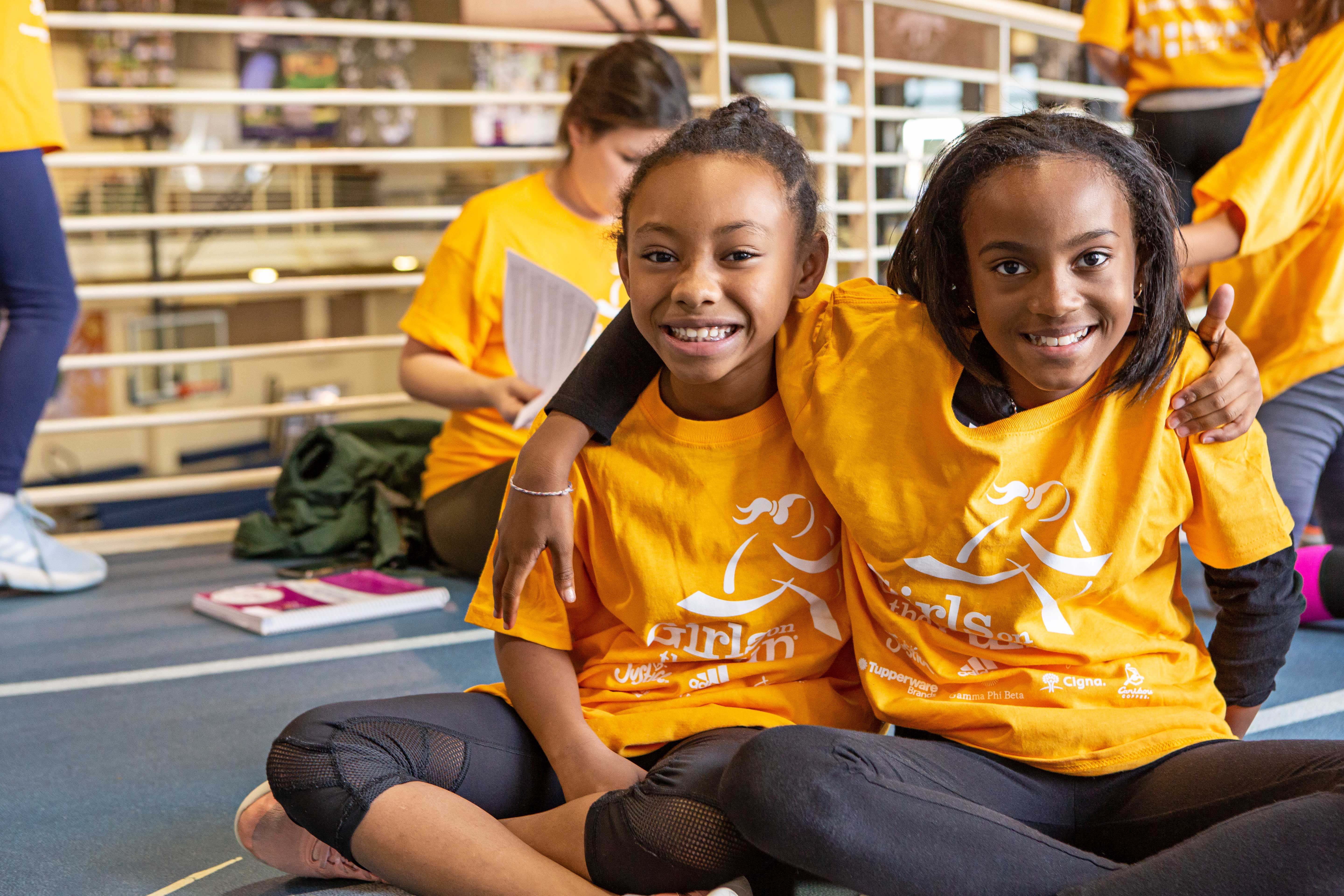 Two Girls on the Run participants in yellow shirts run while smiling at the camera