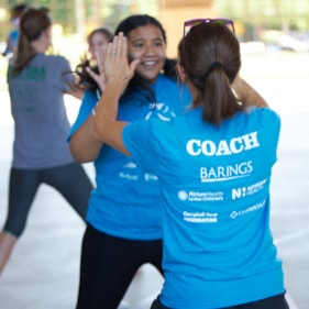 Two Girls on the Run participants high five at an outdoor practice in blue shirts