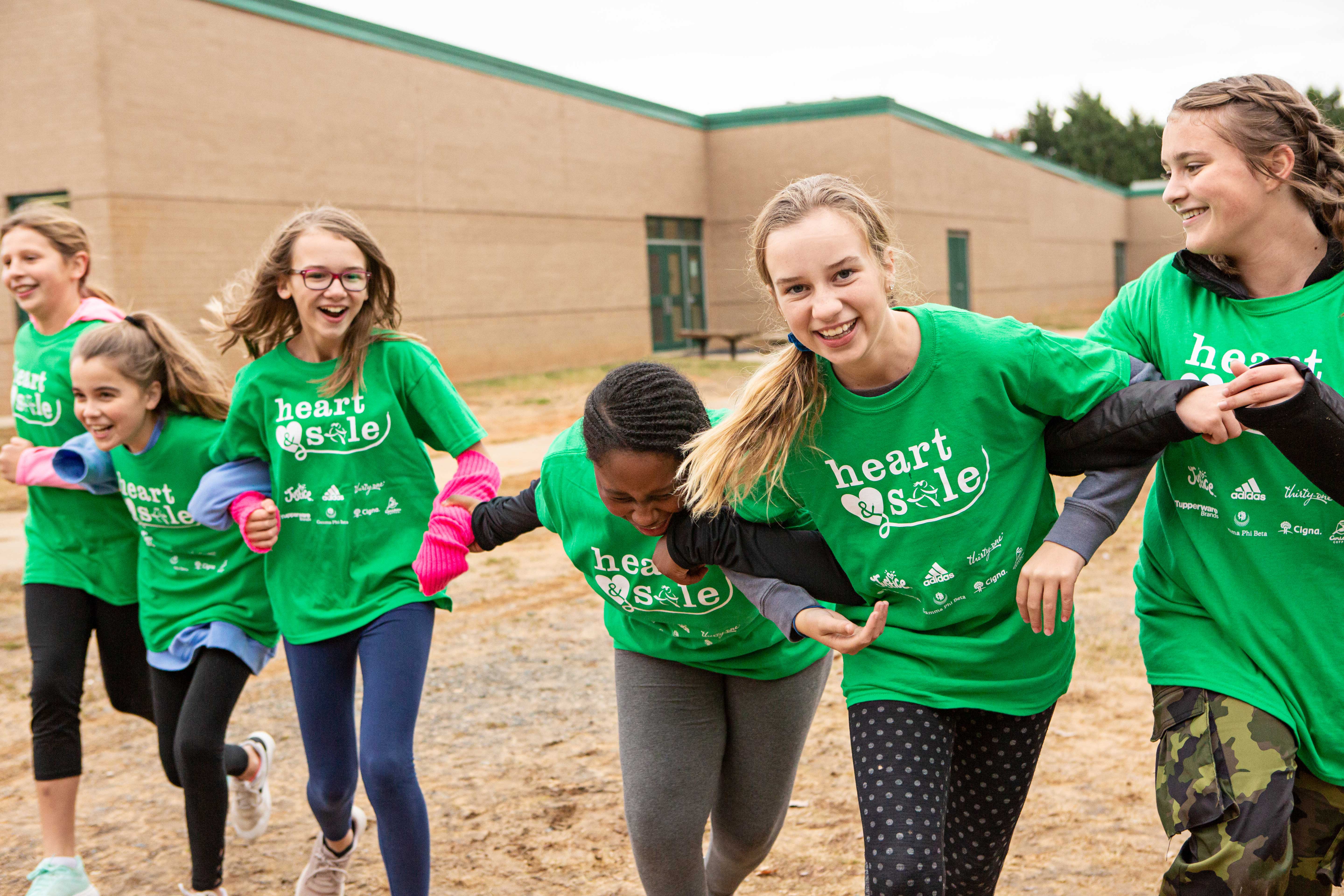 Three Girls on the Run participants smile at the camera while running at an outdoor practice in green shirts
