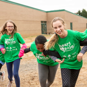 Three Girls on the Run participants smile at the camera while running at an outdoor practice in green shirts